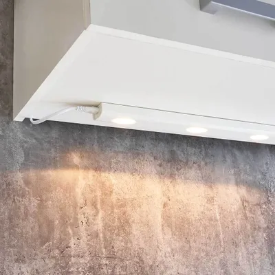 A close-up view of a white LED under-cabinet light fixture with a power cord plugged in.