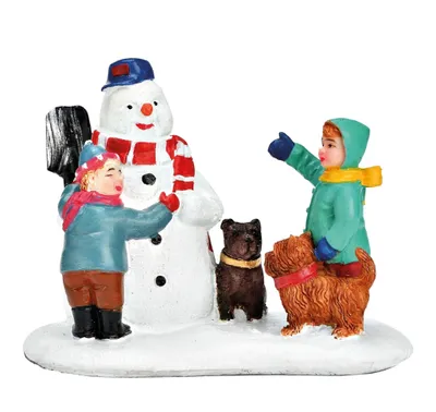 Zwei Kinder haben einen freundlichen Schneemann gebaut. Hunde stehen geduldig neben den Kindern.