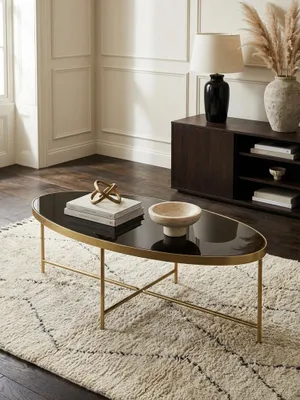 Design Couchtisch oval von oben fotografiert, die glänzende schwarze Glasoberfläche und das filigrane goldene Metallgestell kommen auf dem grauen Teppich zur Geltung._#sku_SAFWL5.993#
