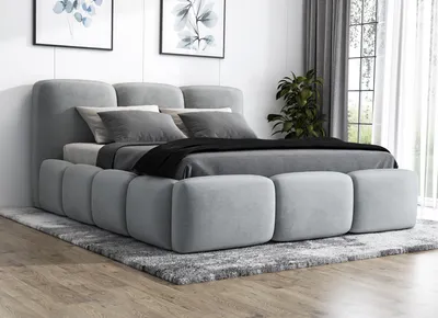 A modern upholstered bed with a headboard and footboard, placed on a rug in a bedroom setting.