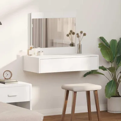 A white dressing table with a mirror, a drawer, and decorative items, placed against a white wall.