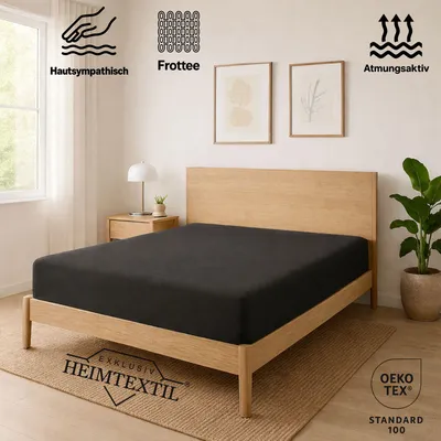 A bedroom scene with a bed featuring a dark gray fitted sheet, a wooden headboard, and a bedside table with a lamp.