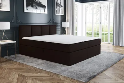 A dark brown box spring bed with a white mattress and topper is shown in a bedroom setting with a gray rug and wooden floor.