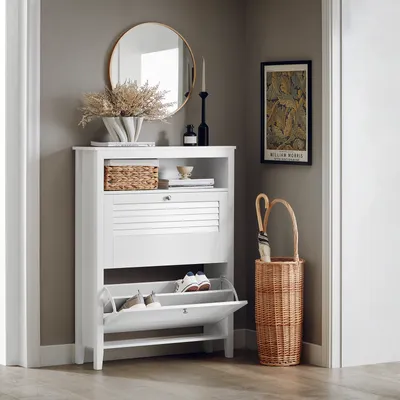 A white shoe cabinet with two flip-down drawers is shown in a hallway next to a woven basket with an umbrella.