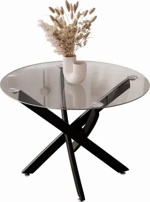 A round glass-top coffee table with a black crisscross base, decorated with a vase of dried flowers.