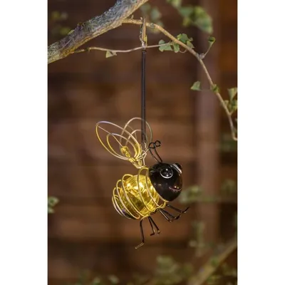 A decorative solar-powered bee lantern hanging from a tree branch.