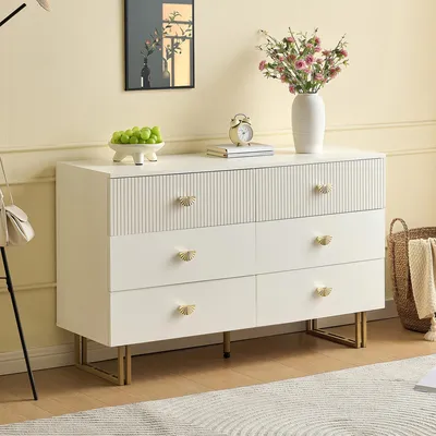 A white dresser with gold accents is shown in a room setting, with decorative items on top.