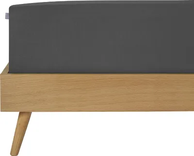 A close-up view of a dark gray fitted sheet on a wooden bed frame with angled legs.