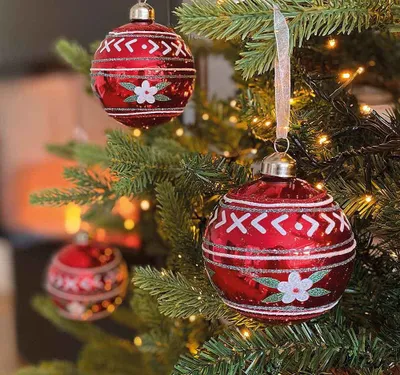 Christmas tree ornaments hanging on a decorated Christmas tree with lights.