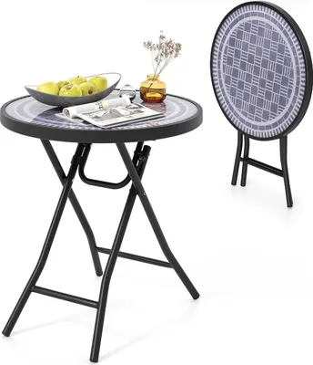 A round folding table with a patterned top, set with a bowl of apples, a glass, and a vase with dried flowers. A second table is shown folded in the background.