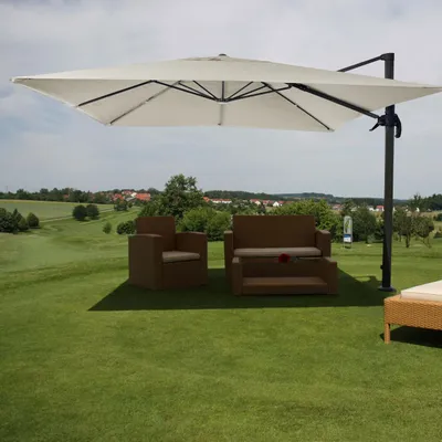 An outdoor patio set with a large cantilever umbrella set up on a grassy lawn, with a town and rolling hills in the background.