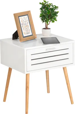A white side table with a drawer and wooden legs, decorated with a framed picture and a small potted plant.
