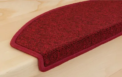 A close-up view of a red carpet stair mat on a wooden stair tread.