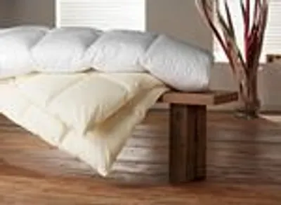 Two duvets are stacked on a wooden bench in a room with blinds in the background.