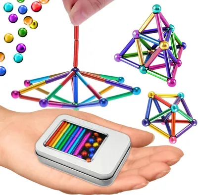 A hand holding a tin of magnetic balls and rods, with several magnetic structures built from them in the background.