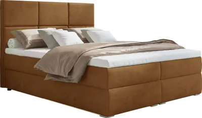 A studio shot of a brown boxspring bed with pillows and a duvet.