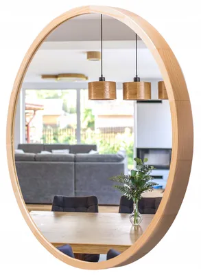 A round wooden mirror reflecting a modern living/dining area with furniture and pendant lights.