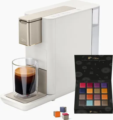 A Tchibo Qbo coffee machine with a glass of espresso and a box of coffee capsules.