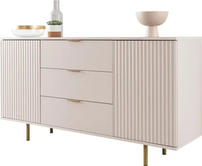 A light-colored sideboard with fluted doors and drawers, set against a white background. Decorative items are placed on top.