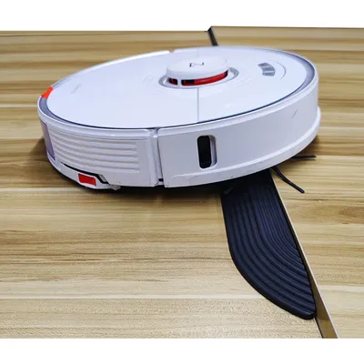 A white robot vacuum cleaner is shown on a wooden floor, with a black transition strip partially underneath it.