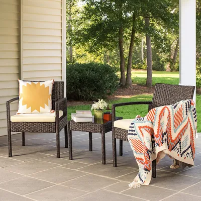 Two chairs and a small table on a patio with trees and bushes in the background.