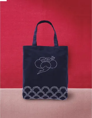 A dark blue tote bag with white embroidery is displayed against a red background and a beige surface.