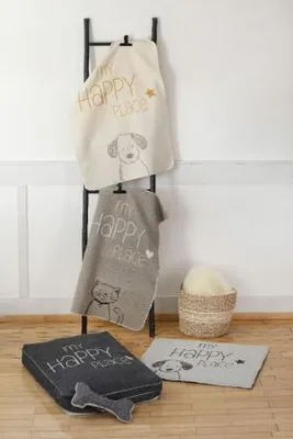 Several pet blankets and a pet bed are displayed on a ladder rack and the floor, with a basket of fluffy material in the background.