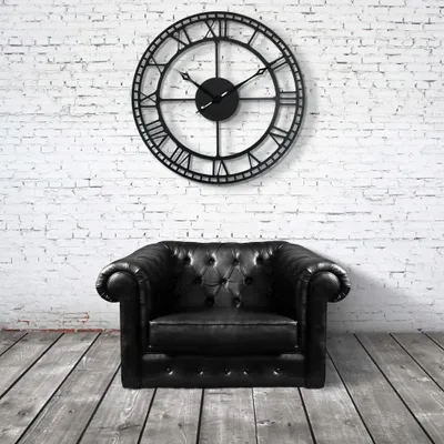 A black leather armchair sits on a wooden floor in front of a white brick wall with a large black clock.