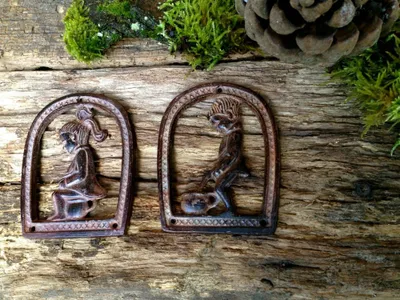 Two rustic metal signs depicting a boy and a girl on a toilet, placed on a wooden surface with moss and a pinecone.
