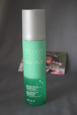 A bottle of Revlon Professional Equave Strengthening Instant Detangling Conditioner is shown against a gray background. A blurred image of a person is visible in the background.