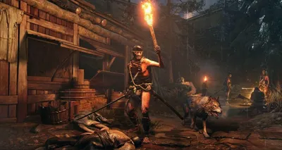A warrior with a torch and a wolf in a dark, rustic village setting.