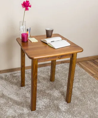 A small wooden table with a flower, candle, notebook, and cup on it, placed on a rug.