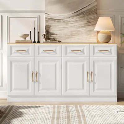 A white sideboard buffet with gold handles, decorated with candles, books, and a lamp, placed in a room with a painting on the wall and a rug on the floor.