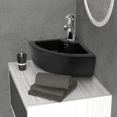 A black corner sink with a chrome faucet is shown on a white vanity with gray towels folded on top.