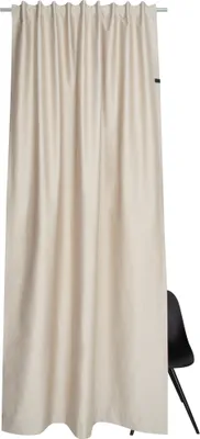 A beige curtain hanging from a rod, with a black chair partially visible behind it.