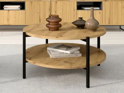 A round, two-tiered coffee table with a wood-grain finish and black metal legs, placed on a light-colored carpet in front of a wooden cabinet.