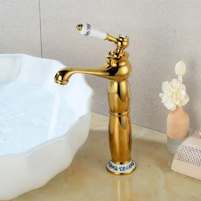 A golden faucet with a white ceramic handle is shown in a bathroom setting, with water flowing into a white sink.