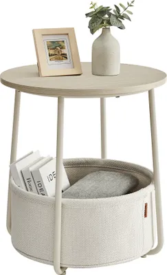 A round side table with a storage basket underneath, decorated with a framed photo and a vase with greenery on top.