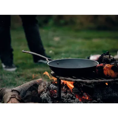 A frying pan is placed over a campfire with food cooking in it. A person's legs are visible in the background.
