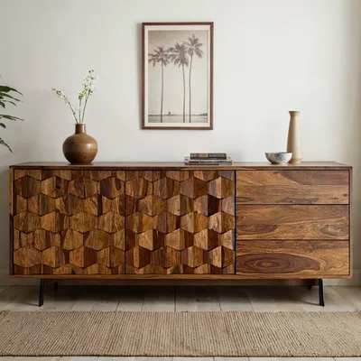 A wooden sideboard with a textured front and drawers, placed on a rug in a room.