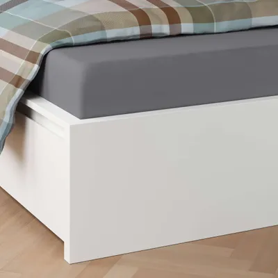 A close-up view of a bed with a grey fitted sheet and a plaid duvet cover.
