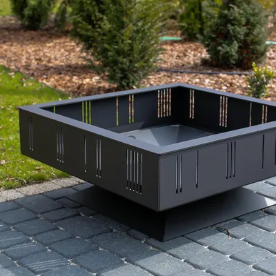 A square metal fire pit sits on a paved patio in a garden setting.