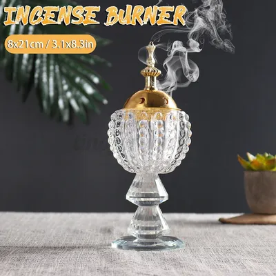 An incense burner with smoke rising from it, placed on a table with a plant in the background.
