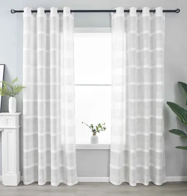 Two white sheer curtains with a horizontal stripe pattern hang on a black curtain rod in front of a window. A white mantelpiece with a vase and plant is visible on the left, and a plant is visible on the right.