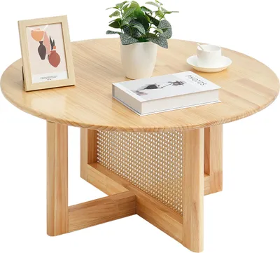 A round wooden coffee table with a woven rattan detail on the lower shelf, decorated with a framed picture, a potted plant, a book, and a teacup.