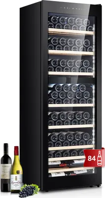 A tall, black wine refrigerator is shown, filled with wine bottles. In front of the refrigerator, three bottles of wine and a bunch of grapes are displayed.