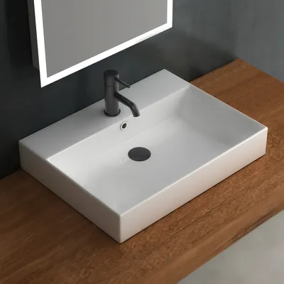 A modern bathroom sink with a black faucet sits on a wooden countertop, with a lit mirror in the background.
