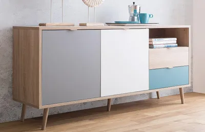 A sideboard with a wood-tone frame and doors in gray, white, and blue, set against a textured wall and wooden floor.
