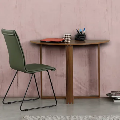 A green chair is placed next to a half-round wooden desk with a laptop, mug, and pen holder on it.