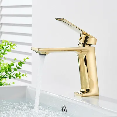 A gold faucet running water into a white sink, with blinds and greenery in the background.